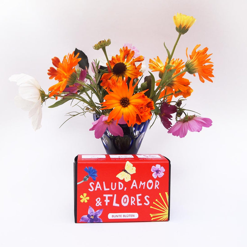 Bio-Blumenkugeln in roter Verpackung mit Blumenstrauss im Hintergrund