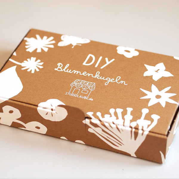 DIY Blumenkugeln Set (Seedbombs) in braunem Karton und weißen Blumen Illustrationen 